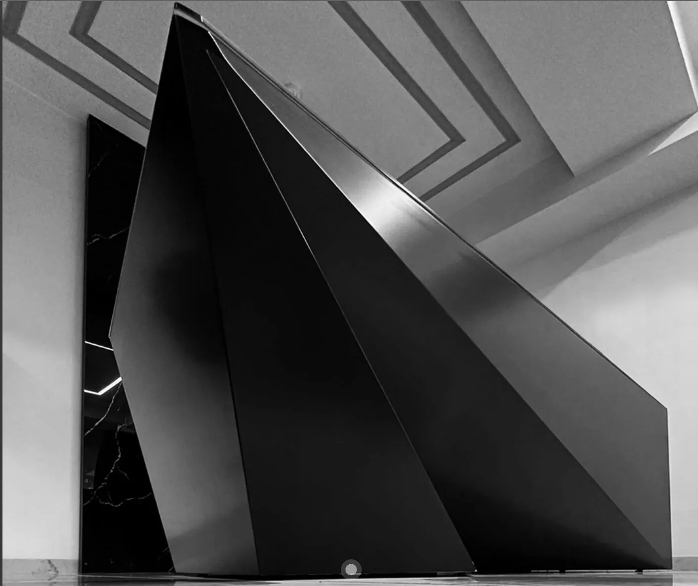 A close view of the desk's large dark planes beneath a geometric ceiling.