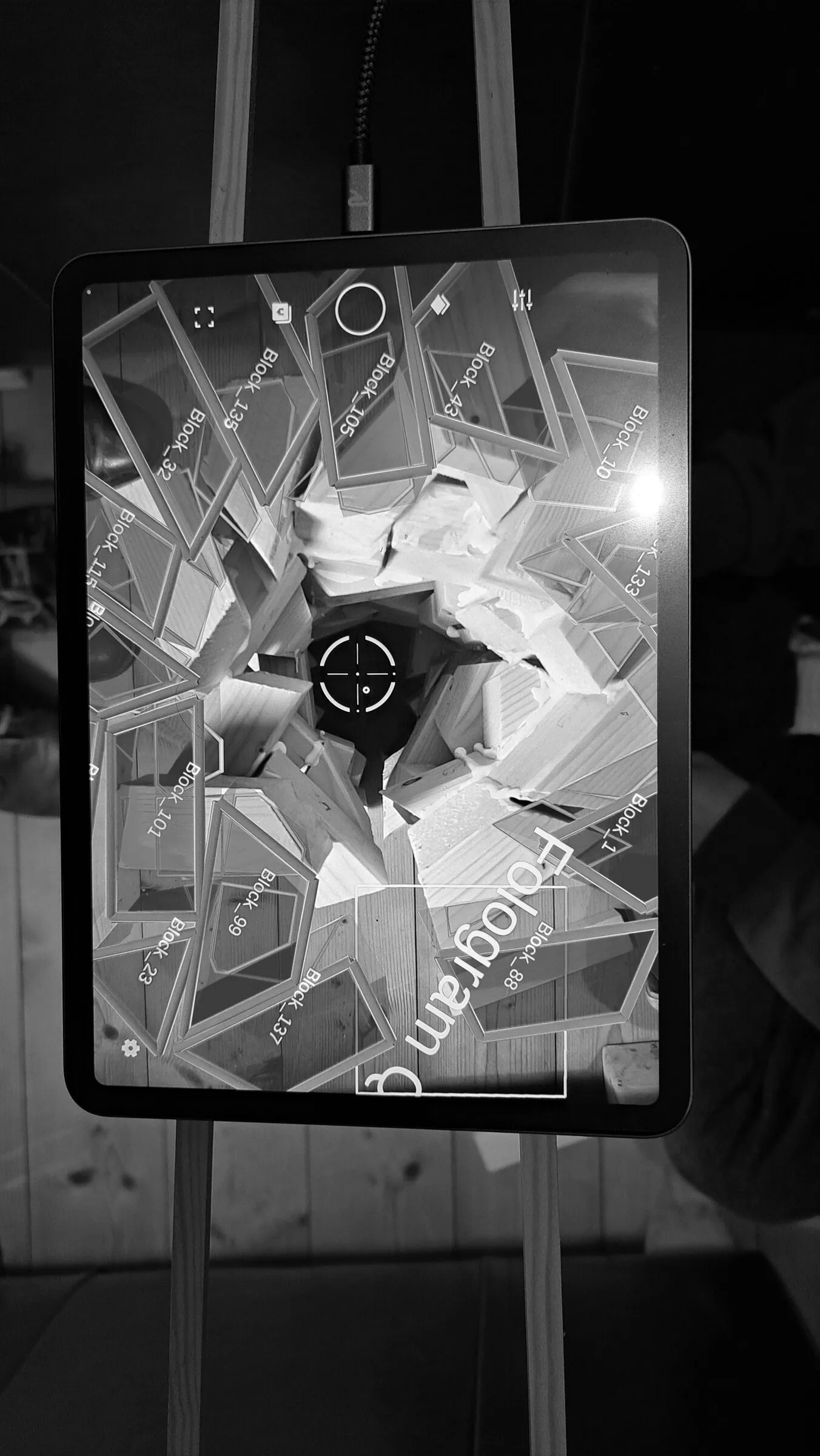 A tablet on a stand shows a block model overlaid on a workshop floor.