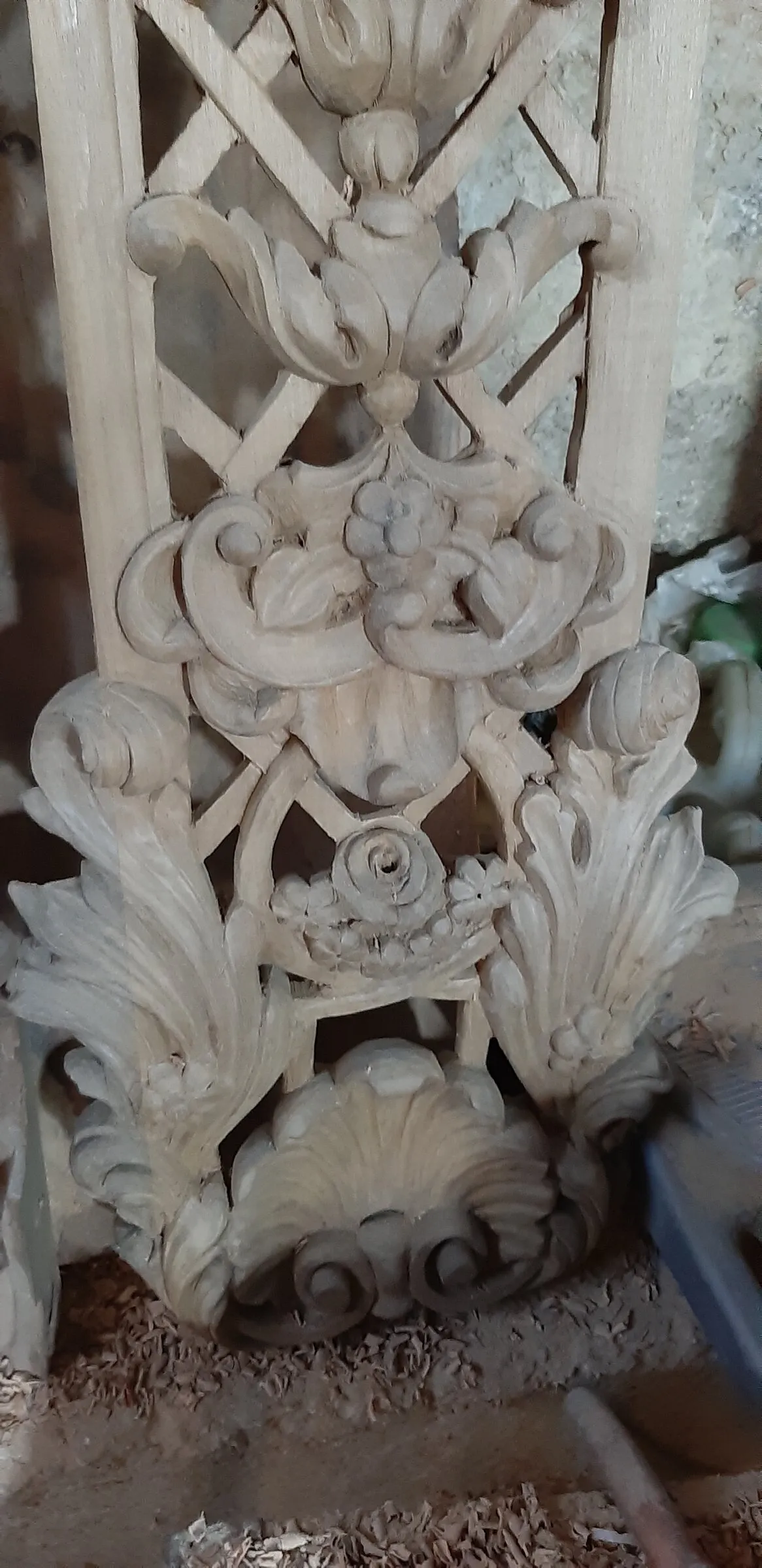 Close view of an unfinished carved relief with repeating leaves and curved stems.