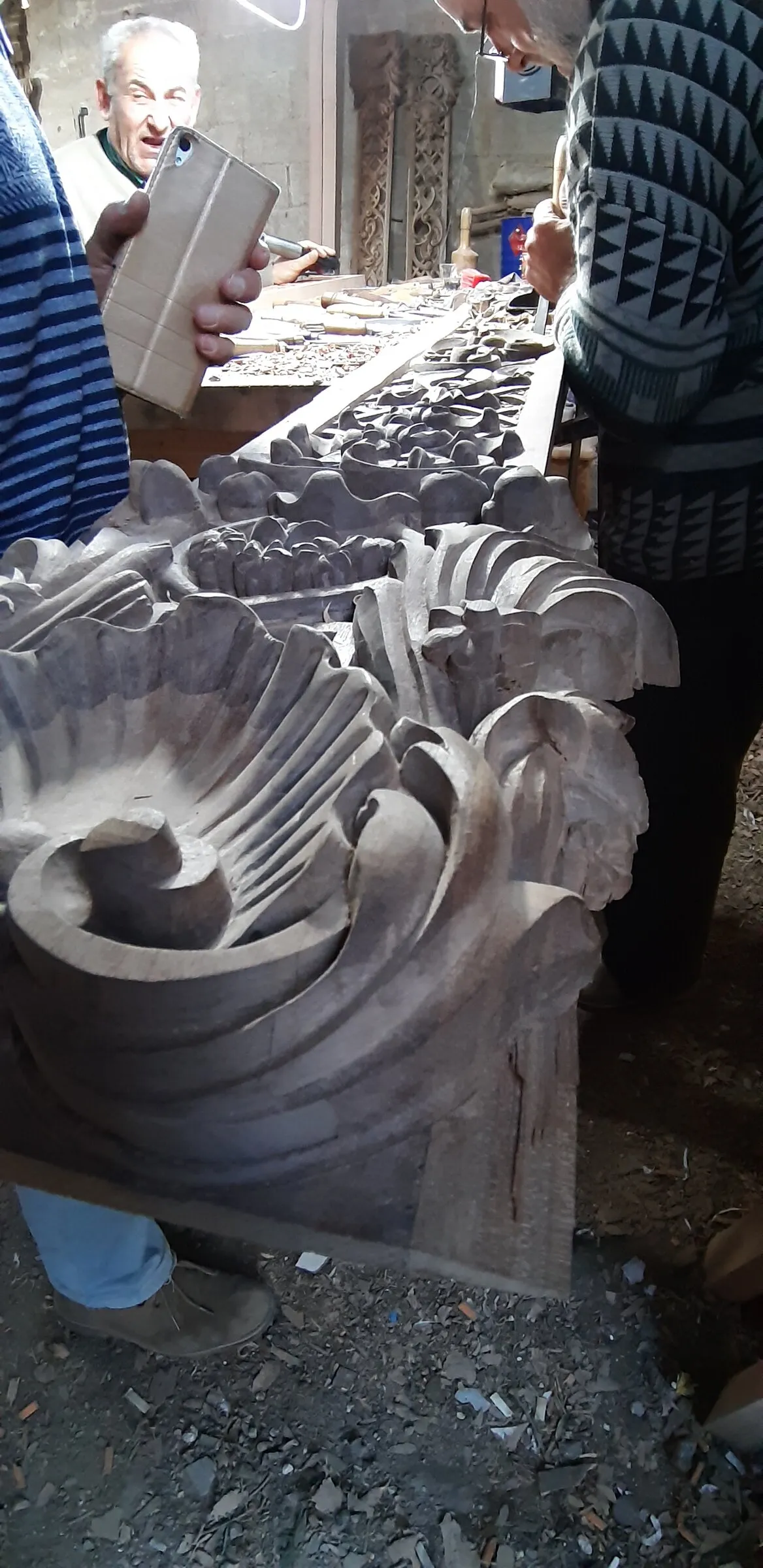 A worker stands beside a long carved panel in a timber workshop.