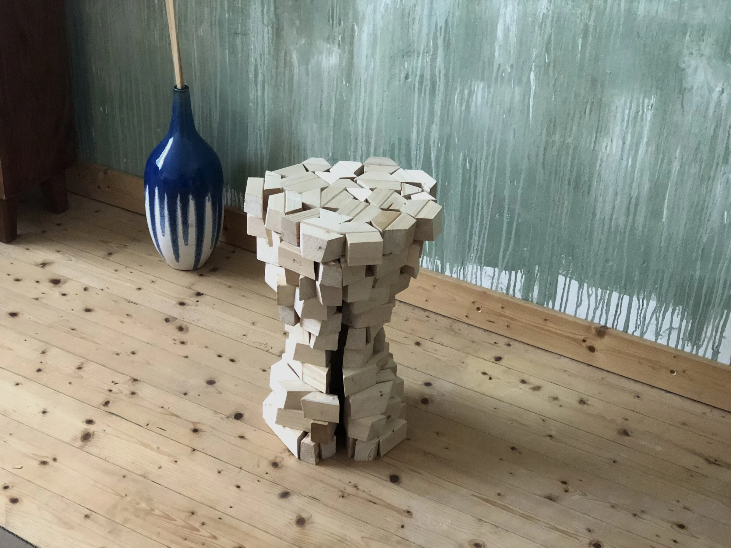 A twisting stool made from stacked wooden blocks stands on a workshop floor.