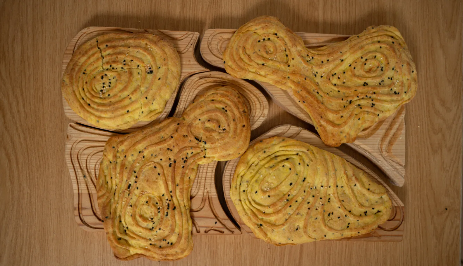 Seeded oval breads rest on carved wooden moulds across a wooden table.