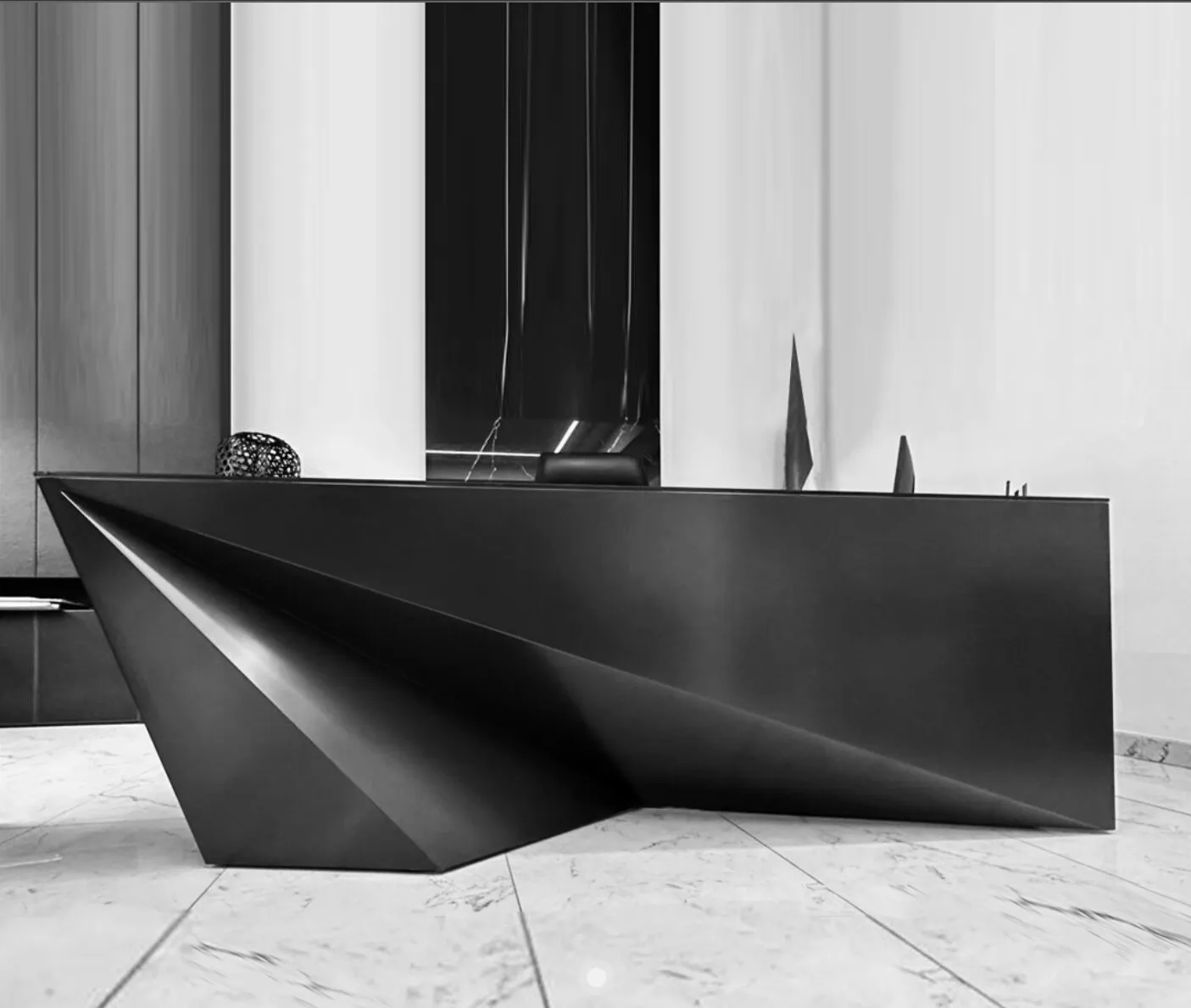 A dark angular desk with folded planes stands in a marble-floored office.